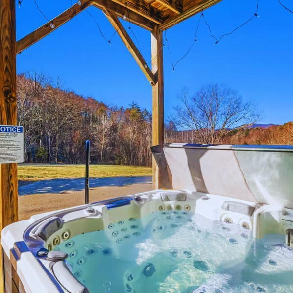 A hot tub under a wooden pergola with a clear view of trees and mountains in the background.
