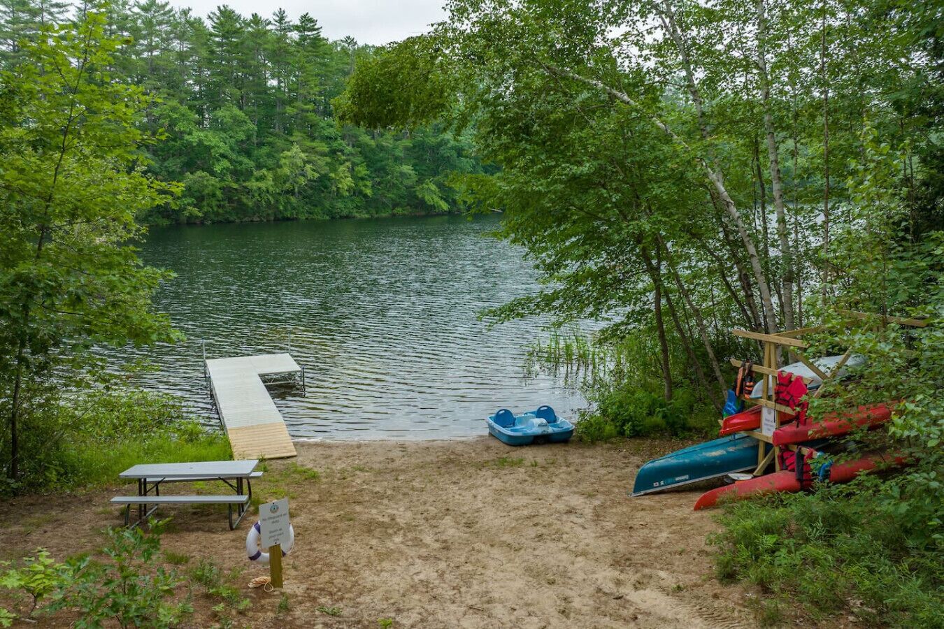 Un entorno junto al lago con un muelle, una mesa de picnic y canoas.