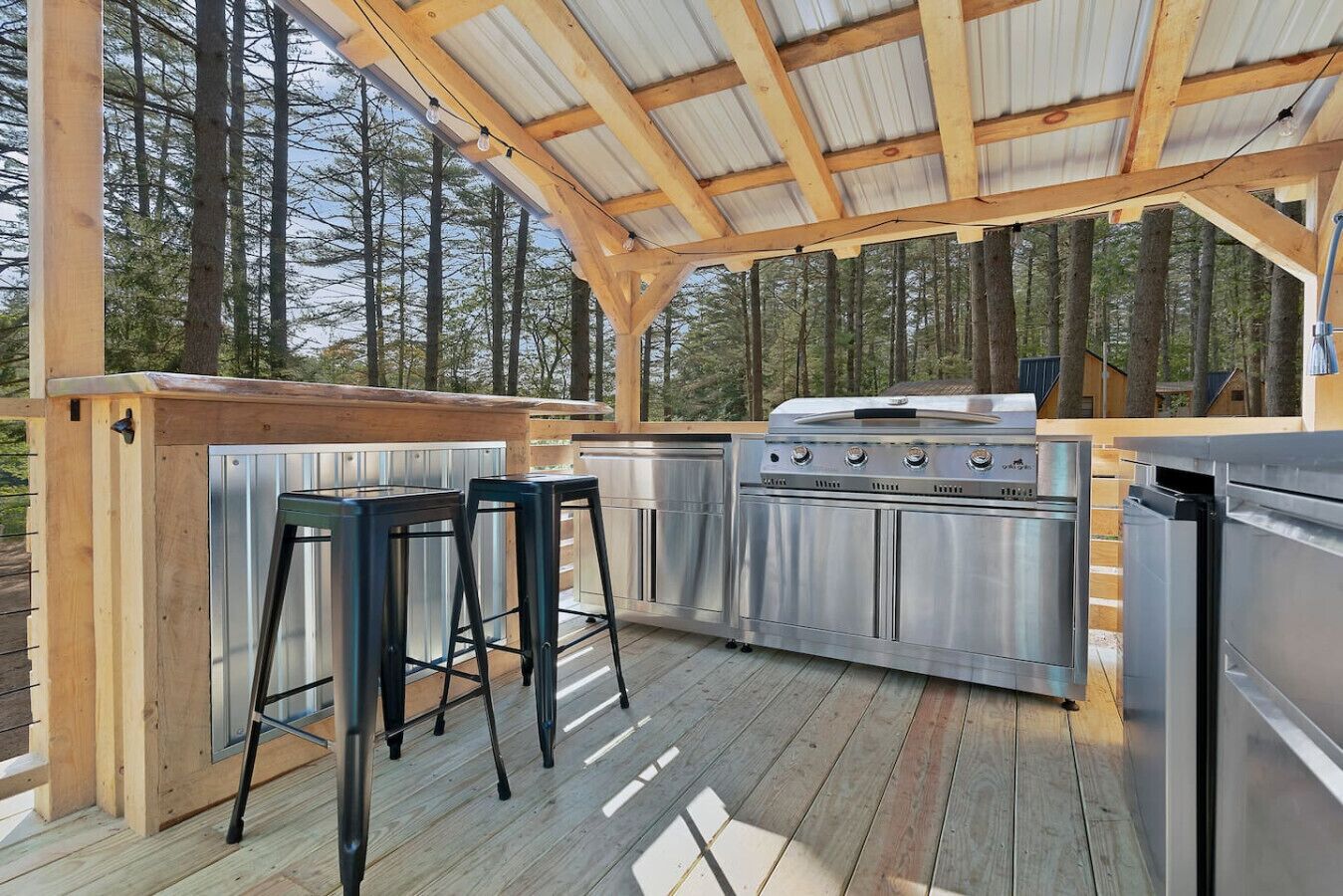 Una cocina exterior con una parrilla, taburetes de bar y una terraza de madera.