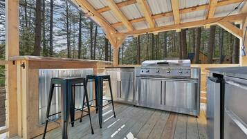 Una cocina exterior con una parrilla, taburetes de bar y una terraza de madera.