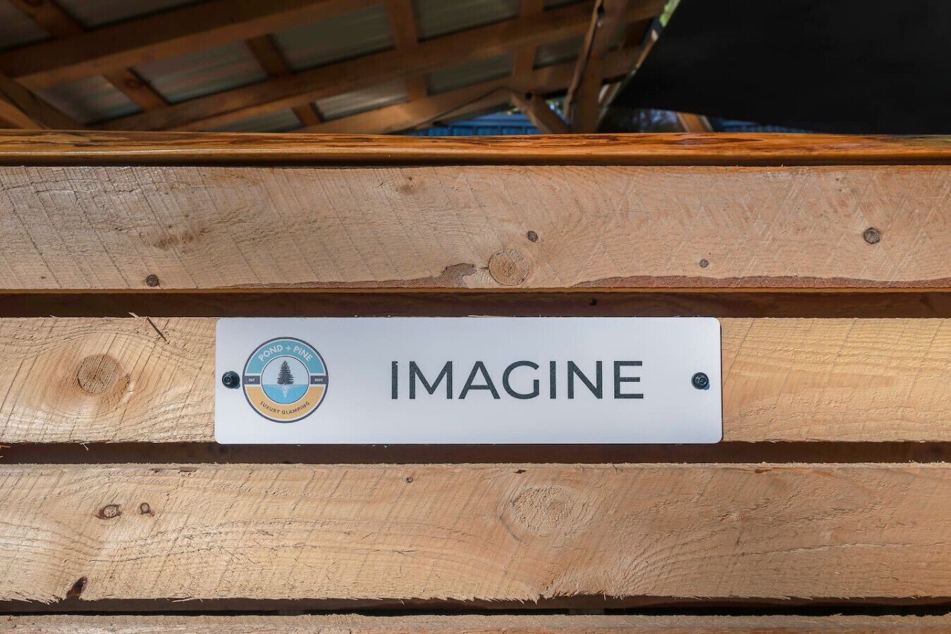 A wooden structure with a sign that reads "IMAGINE" and a logo with the text "POND + PINE" and "EST 2003".