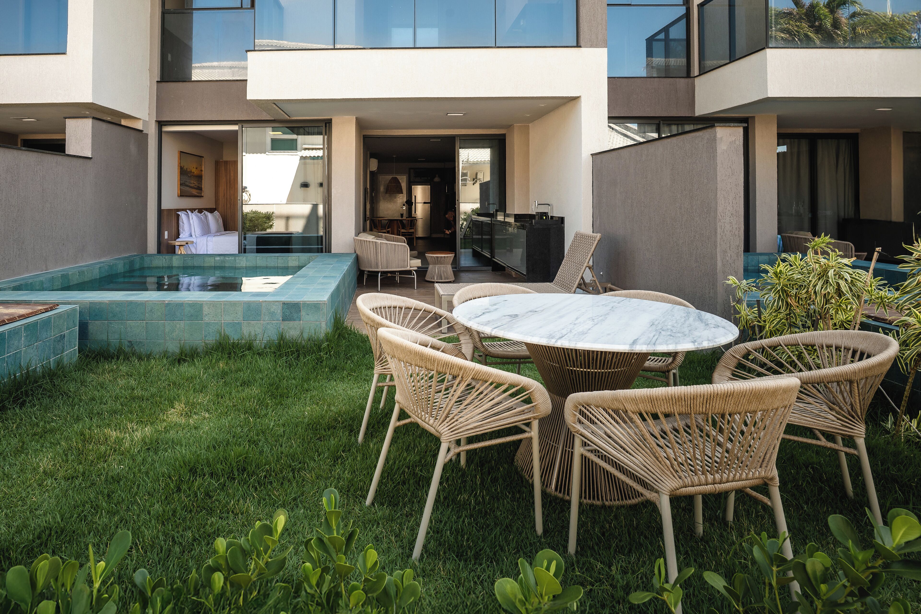 Un patio moderno al aire libre con piscina, muebles de mimbre y cocina con paredes de vidrio.