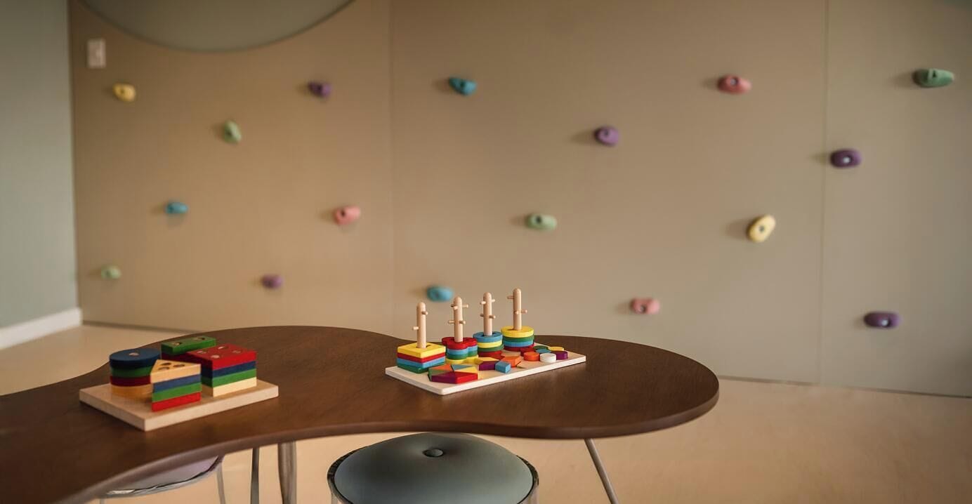 A table with colorful wooden blocks and a pegboard wall in the background.