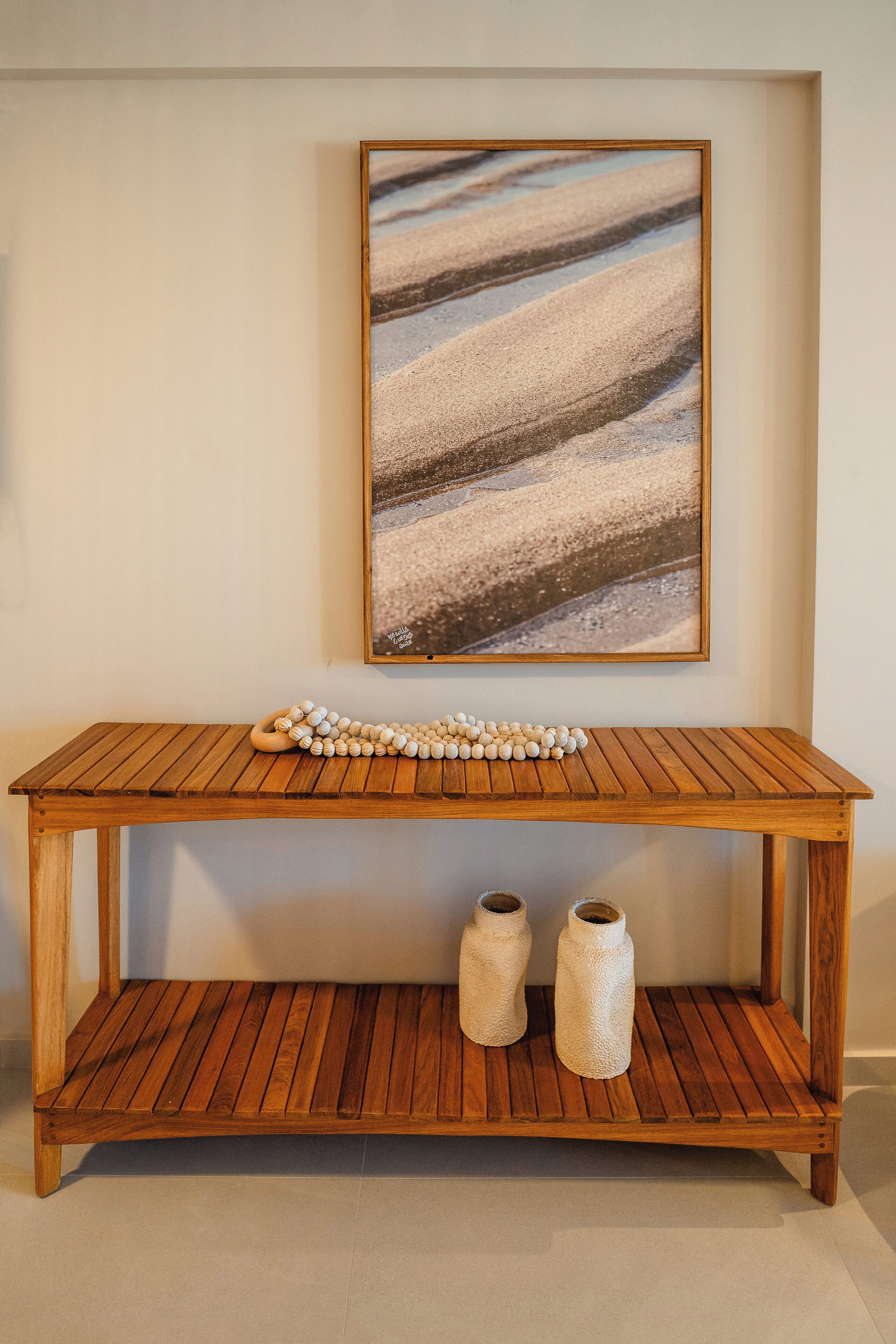 A wooden console table with a framed abstract painting above it and two textured vases on the lower shelf.