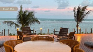 Een strandbar met een ronde tafel en stoelen, palmbomen en uitzicht op de oceaan.