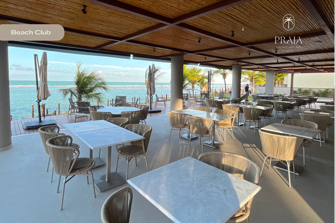 A beach club with outdoor seating, tables, and umbrellas, overlooking the sea.