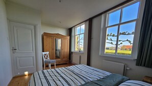 Quarto com cama grande, armário de madeira, cadeira e janela com vista para vegetação.