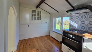 Cozinha com piso de madeira, armários brancos, forno preto e vista para o verde lá fora.