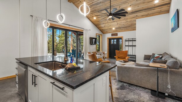 Una cocina moderna con una isla grande, armarios blancos y un comedor con sofá gris y sillón naranja.