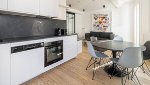 A modern kitchen with white cabinetry, a black countertop, and a built-in oven. There is a dining area with a round table and chairs. - Villa Royale - Luxurious 3 bedrooms near Croisette (Cannes)