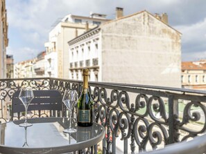 Une table avec une bouteille de champagne et deux verres, placée sur un balcon donnant sur une vue panoramique de la ville.