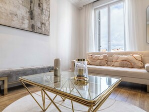 Ein modernes Wohnzimmer mit einem Glastisch, einer Couch mit Zierkissen und einem großen abstrakten Gemälde an der Wand.