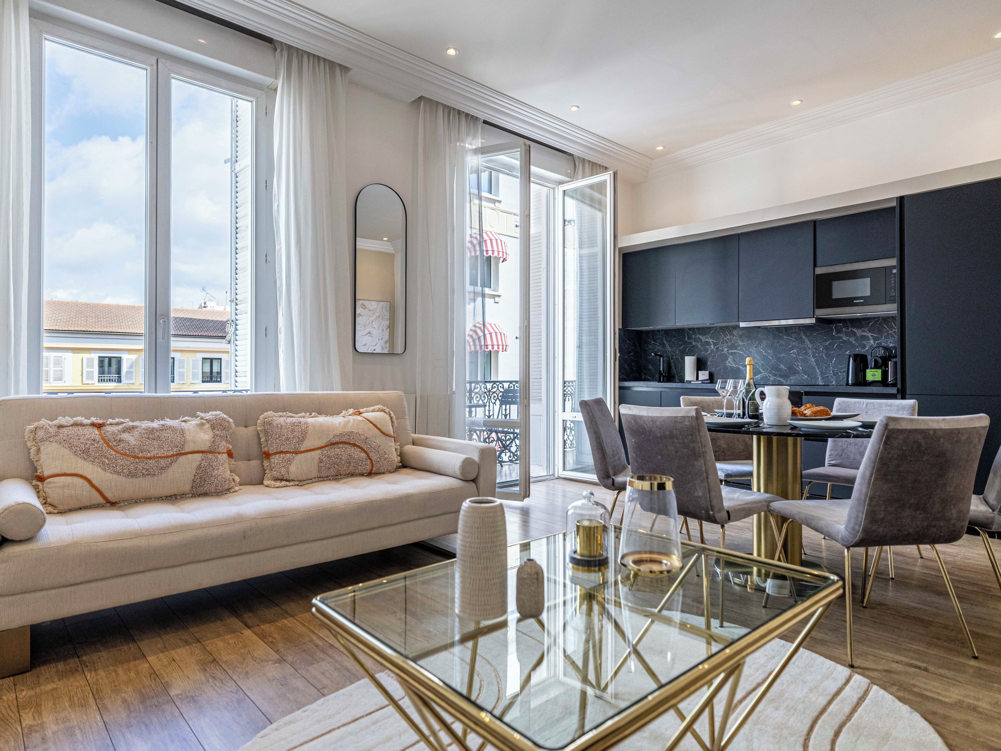 Una sala de estar moderna con una mesa de centro de vidrio, un sofá con almohadones decorativos y vistas de la ciudad a través de amplias ventanas.
