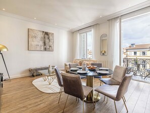 Ein modernes Wohnzimmer mit einem runden Esstisch, bequemen Sitzmöglichkeiten, einem großen abstrakten Gemälde und Blick auf die Stadt durch die Fenster.