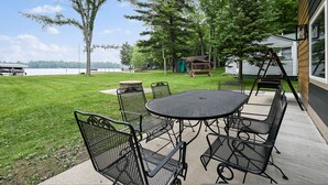 Une terrasse avec une table ronde et des chaises, une balançoire et une vue sur un lac.