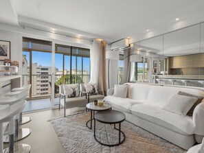 Ein modernes Wohnzimmer mit Sofa, Sesseln, einem Couchtisch und Blick auf die Stadt durch große Fenster.