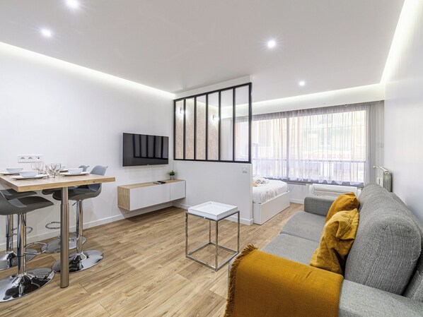 Een moderne woonkamer met een bank, een eettafel en een aan de muur bevestigde televisie.