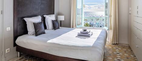 A hotel room with a large bed, a view of the city through a window, and a patterned floor.