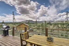 Eine Holzdiele mit Grill und Tisch, mit Blick auf eine gebirgige Landschaft.