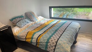 A bedroom with a bed, a nightstand, a window, and a view of greenery outside. - Modern house near the sea (Trébeurden)