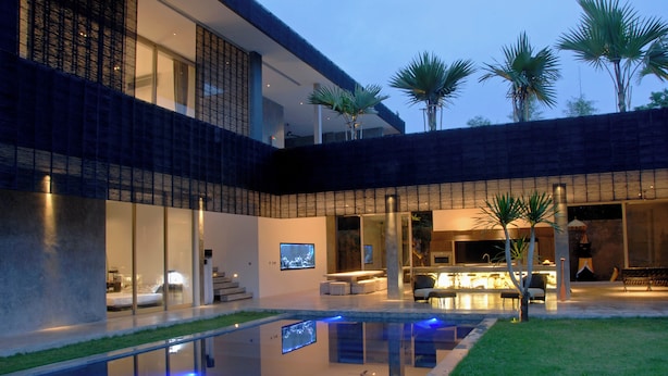 Ein modernes Haus mit Swimmingpool, Sitzgelegenheiten im Freien und Palmen.