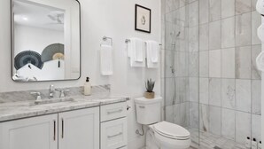Un baño moderno con lavamanos de mármol, inodoro y cabina de ducha de vidrio.