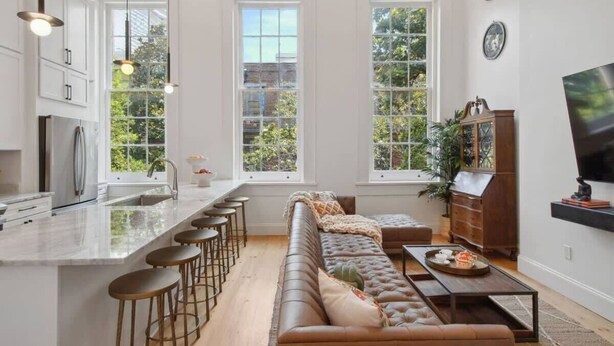 Una cocina moderna con una isla central, taburetes de bar, un sofá de cuero y una mesa de comedor.