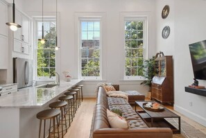 A modern kitchen with a central island, bar stools, a leather sofa, and a dining table.