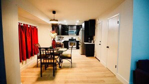 Una cocina compacta con electrodomésticos modernos, un comedor con mesa y sillas, y un pasillo con una puerta.