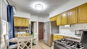 Een keuken met houten kasten, een roestvrijstalen koelkast, een gasfornuis en een eethoek met een tafel en stoelen.