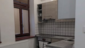 A compact kitchen with a built-in oven, a small countertop, and a window with blinds.