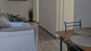 A modern living room with a flat-screen TV, a sofa, a dining table with chairs, and a large window.