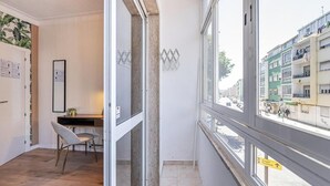 A hotel room with a desk, chair, and large windows offering a view of the street. - Goa Square Guesthouse by Lisbon with Sintra (Amadora)