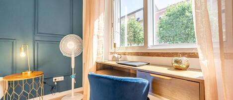A room with a desk, a chair, a standing fan, and a lamp.