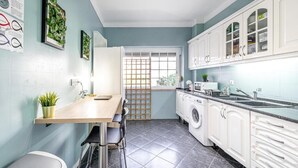A modern kitchen with white cabinets, a wooden countertop, and a sink. There are plants on the wall and a window with a view. - Goa Square Guesthouse by Lisbon with Sintra (Amadora)