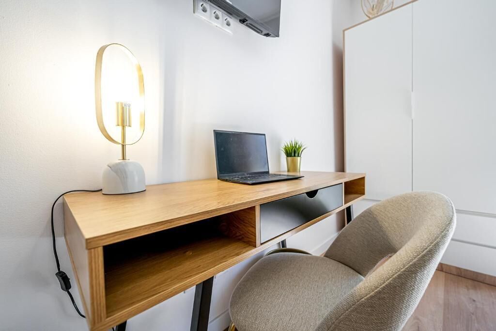 Een houten bureau met een laptop, een plantje en een moderne lamp.