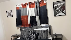 Ein Schlafzimmer mit einem Bett, zwei Nachttischen, einem gerahmten Bild und einem Vorhang.