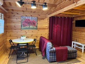 Une pièce chaleureuse avec un décor intérieur en bois, une table ronde entourée de chaises, un canapé et un rideau rouge.