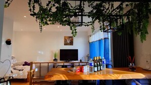 Uma sala de estar moderna com uma mesa de jantar de madeira, uma televisão de tela plana e uma grande janela com cortinas azuis.