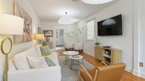A living room with a sofa, coffee table, chairs, a TV, and a cabinet. - Historic Uptown New Orleans 2BR – 1 Block to St. Charles Streetcar (New Orleans)