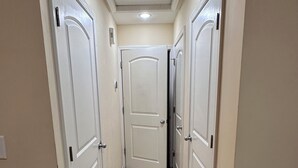 Un corridoio con pavimenti in moquette e porte bianche su entrambi i lati, che conduce a una stanza con una luce a soffitto.