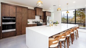 Een moderne keuken met donkere houten kastjes, roestvrijstalen apparatuur, een groot eiland met barkrukken en hanglampen.