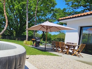 Un patio exterior con una parrilla, un paraguas grande y una mesa de comedor con sillas.