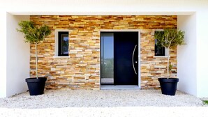 A modern building facade with a stone-textured wall, two small windows, and two potted plants. - Villa, close to beaches (Pornic)