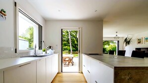 A modern kitchen with white cabinetry, a large window, and a view of the outdoors. - Villa, close to beaches (Pornic)