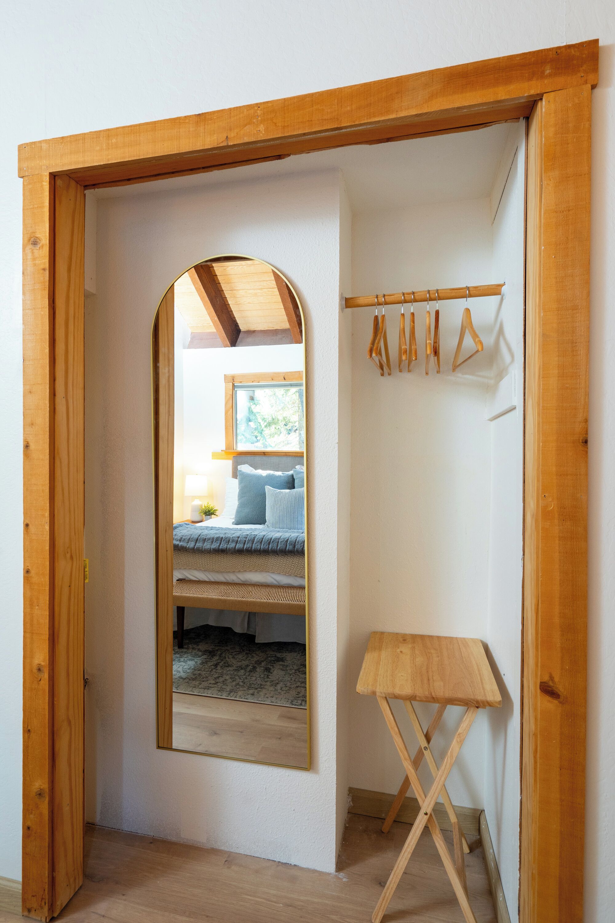 Une pièce avec un cadre de porte en bois, un lit avec une literie bleue, une petite table en bois et un porte-manteau avec des cintres.
