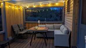A cozy outdoor seating area with a wooden deck, a cushioned sofa, and two chairs. - Modern, cozy tiny house with covered terrace (Thaining)