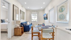 Una sala de estar moderna con un sofá azul, una mesa de comedor redonda con sillas, una pequeña mesita de madera y un televisor montado en la pared.