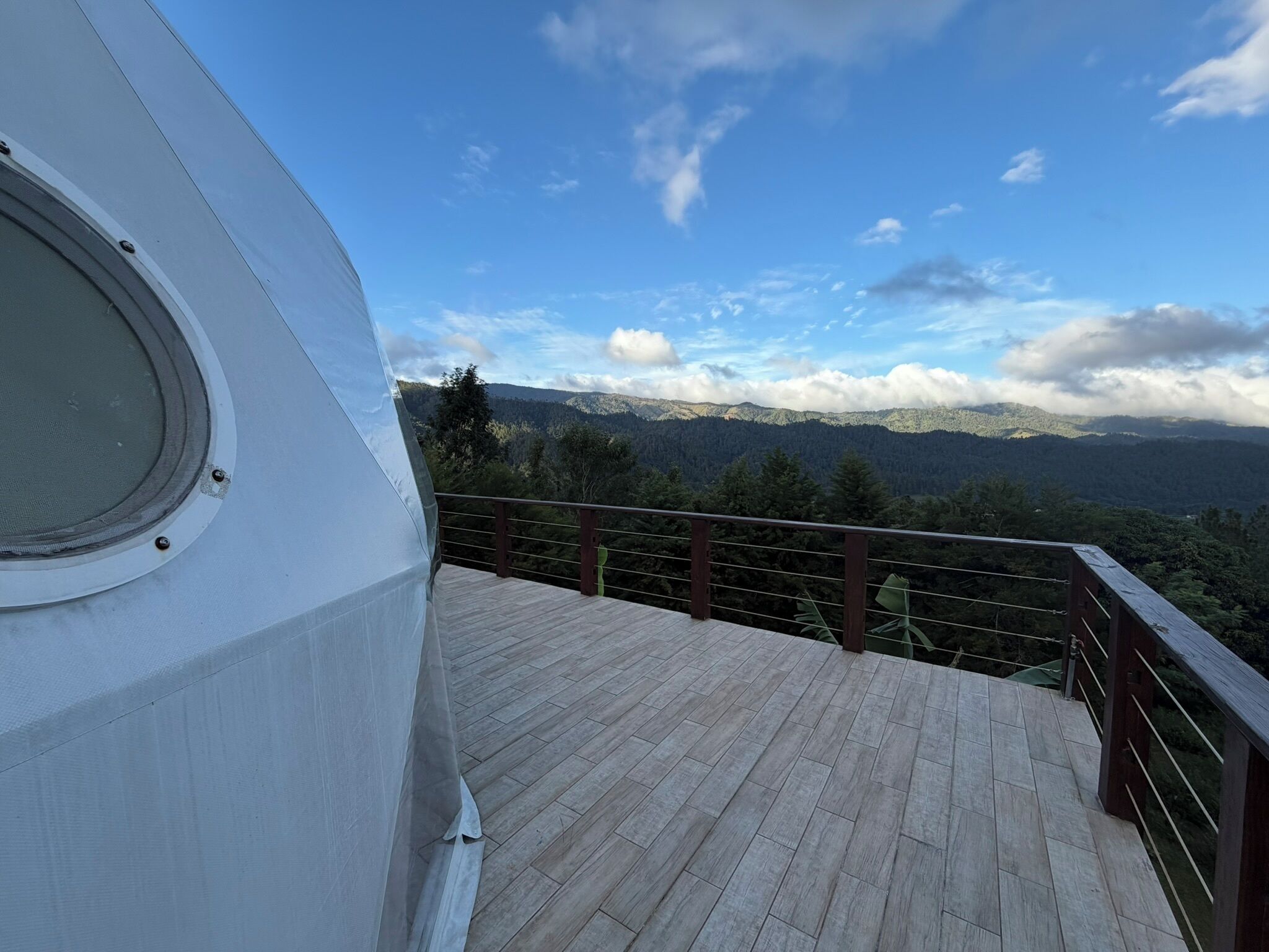 A balcony with a wooden floor and a metal railing overlooking a mountainous landscape.