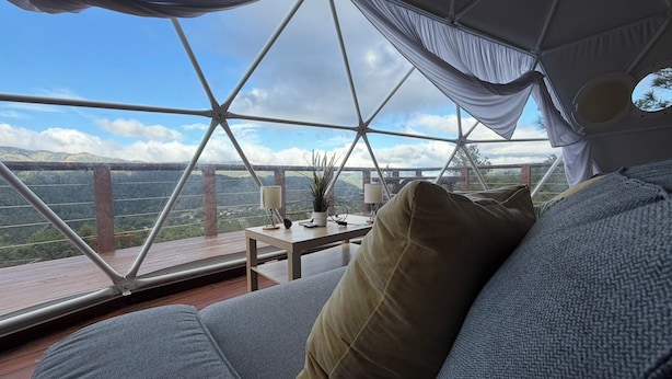 Una habitación acogedora con vistas a un paisaje montañoso, una mesa de madera con una lámpara y un sofá cómodo.